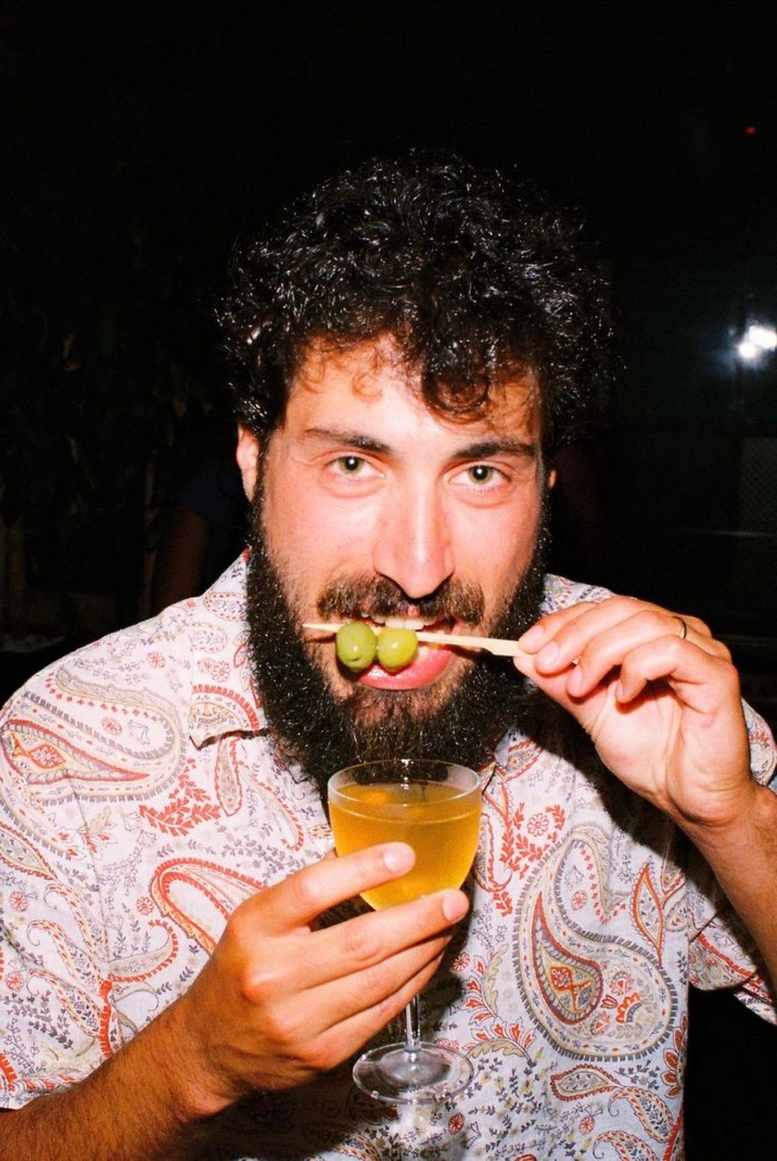 Guest in a paisley shirt raising a martini and an olive skewer at Margolis