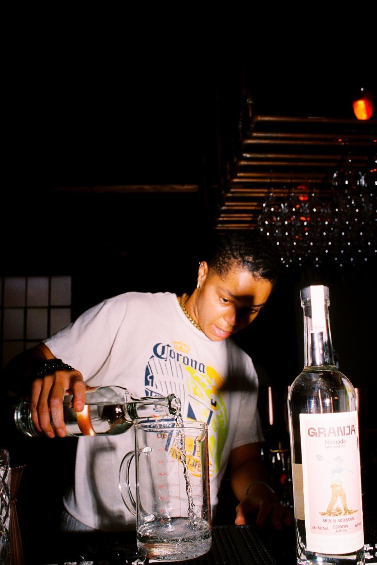 Bartender pouring tequila into a mixing glass beneath the hanging stemware rack
