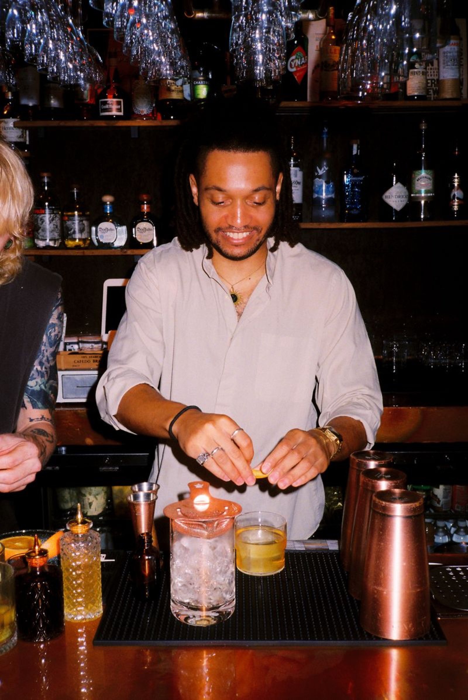 Bartender garnishing a cocktail behind the copper-topped bar at Margolis
