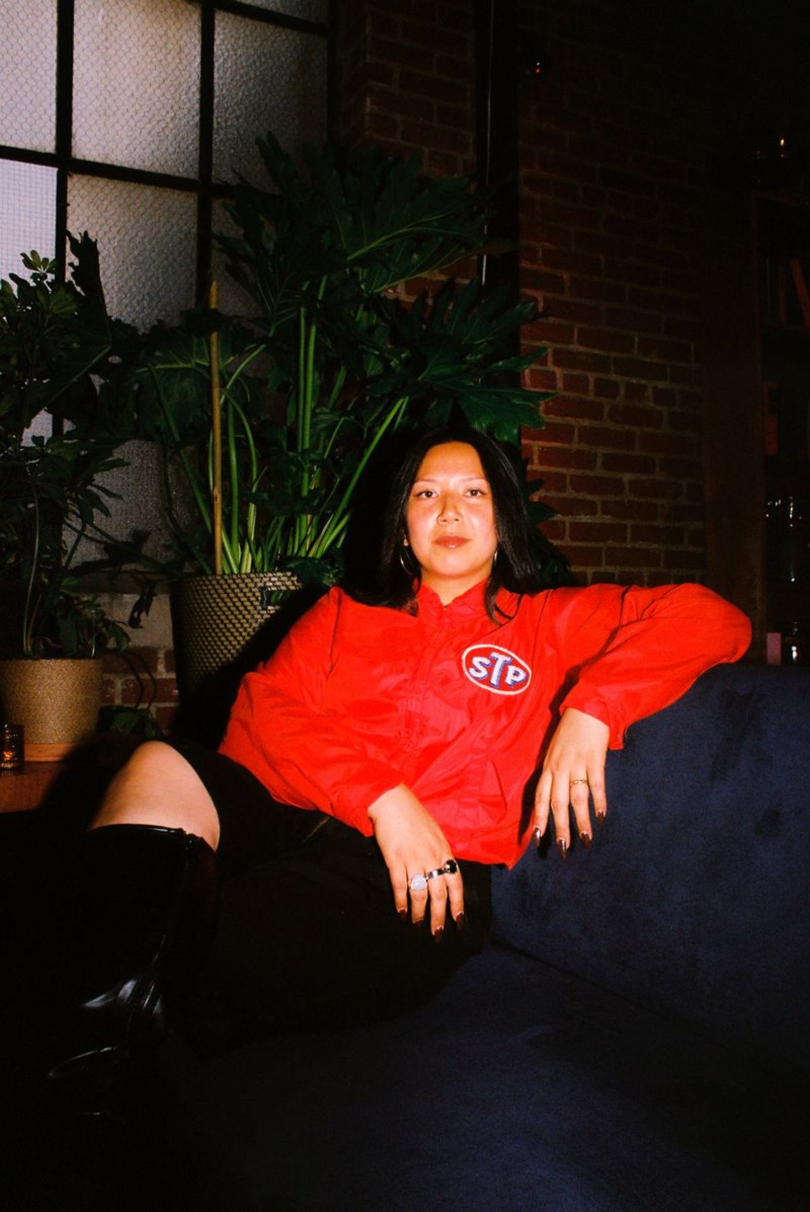 Guest in a red racing jacket on a velvet sofa beside the brick wall and plants