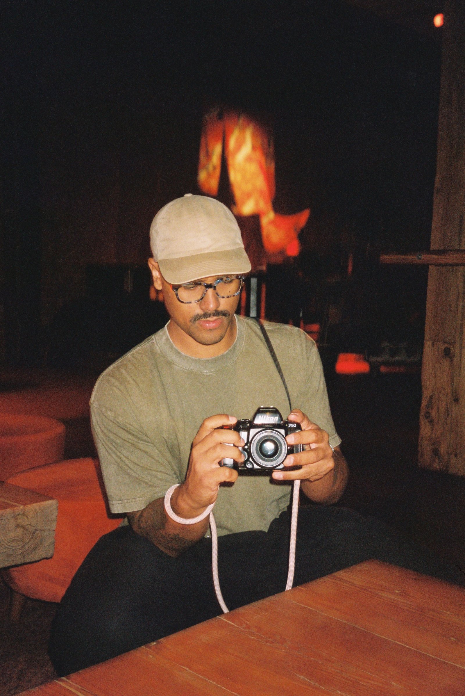 Guest with a film camera at a low wood table, the fireplace glowing behind