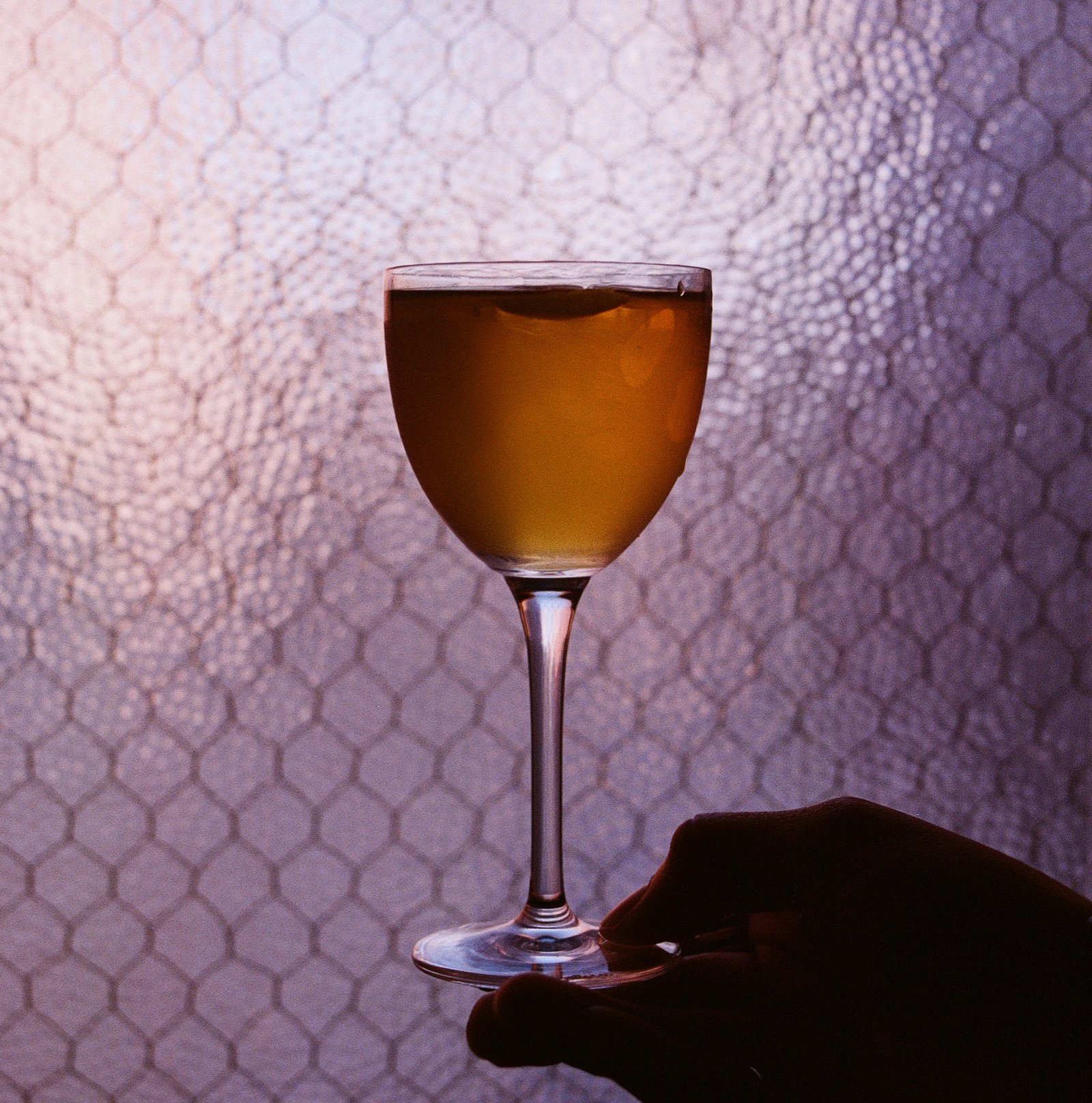 Amber cocktail in a stemmed glass held up against the mesh-patterned window