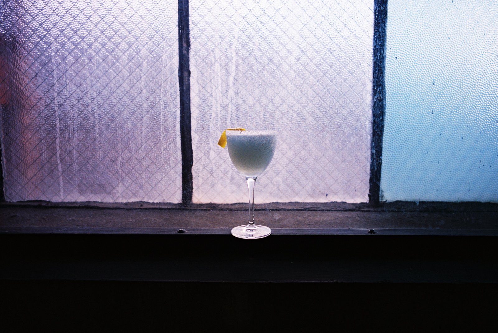 Pale cocktail with a lemon twist on the windowsill in fading evening light