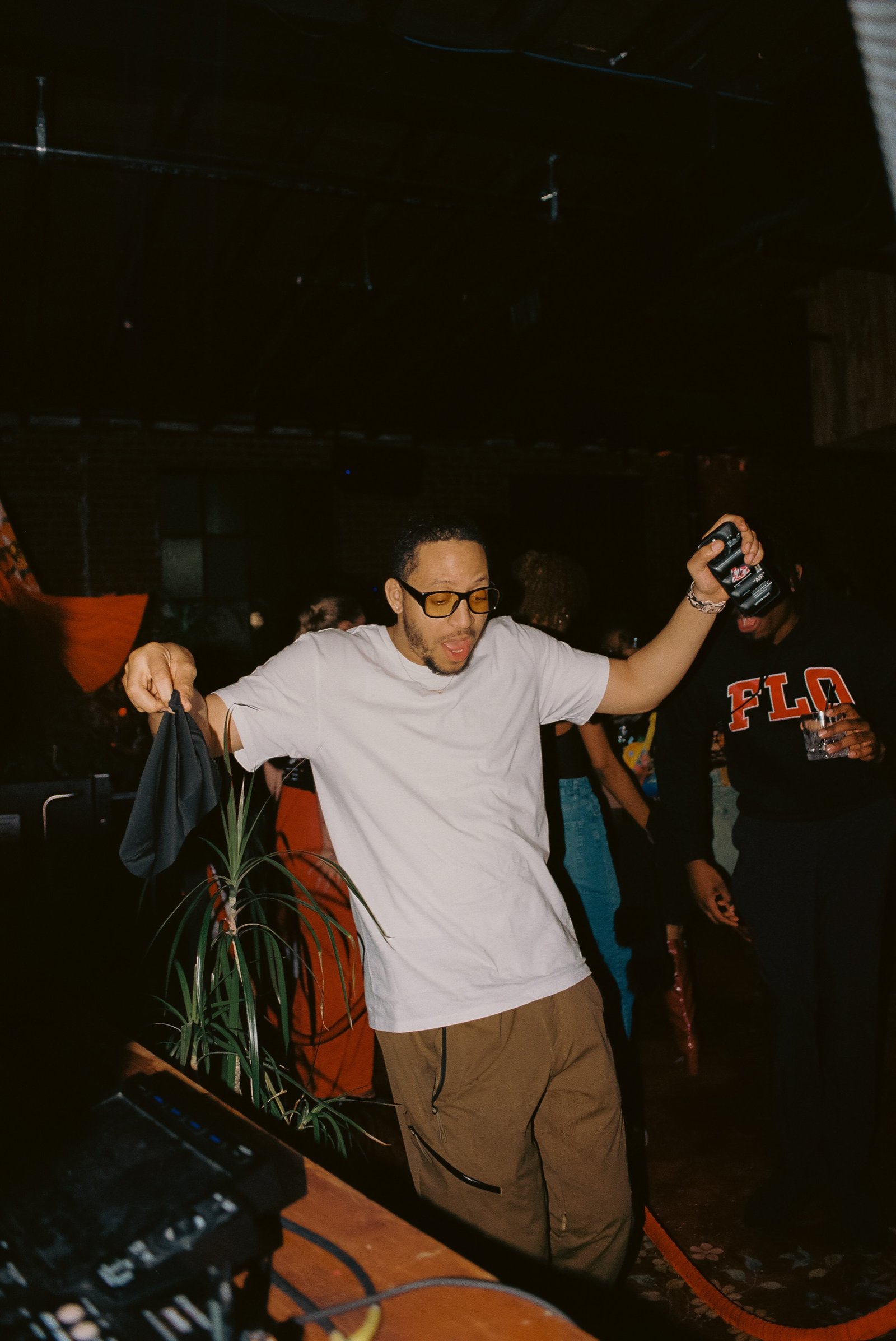 Guest dancing with a drink raised beside the DJ booth at Margolis