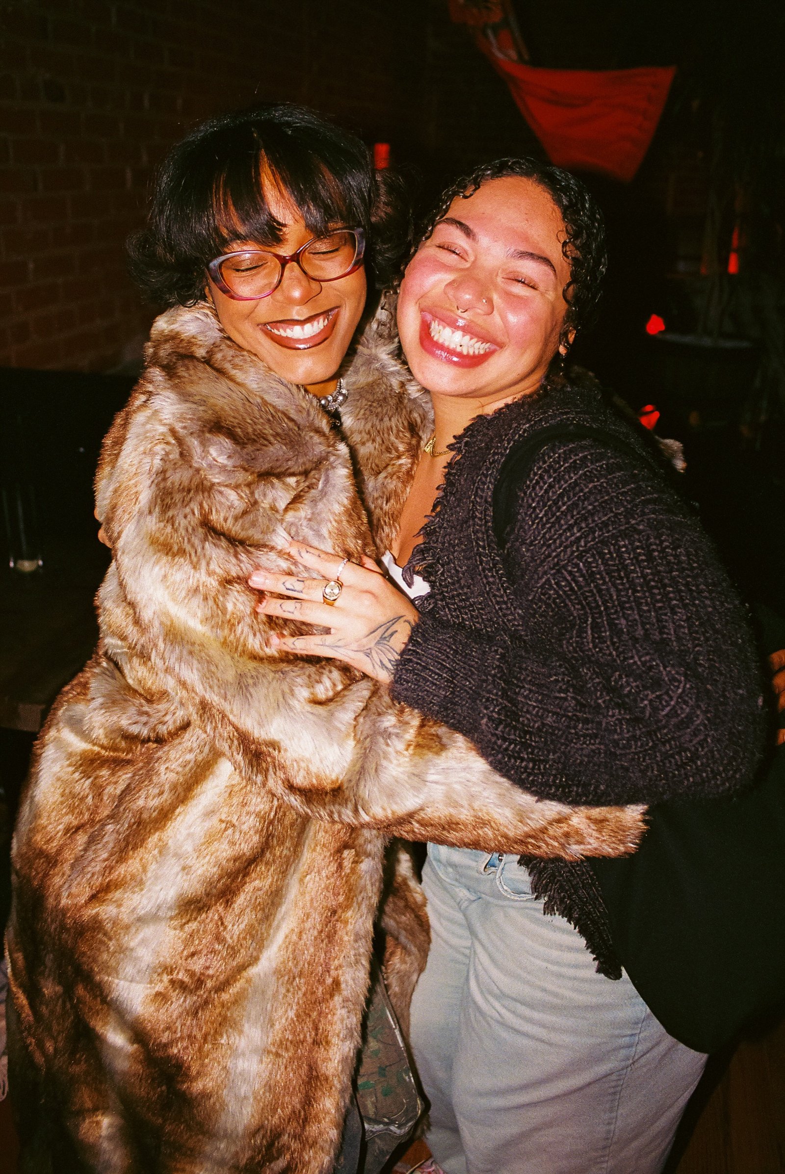 Two guests laughing mid-hug, one wrapped in a fur coat