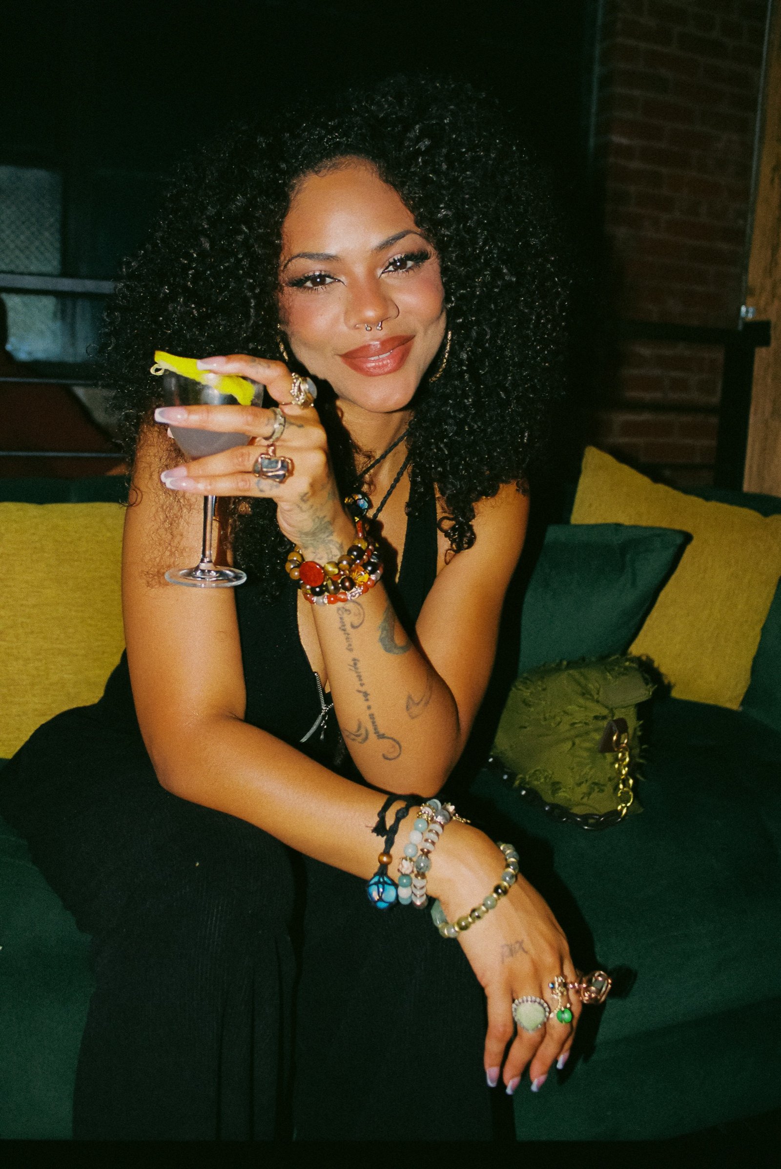 Guest with a martini seated on the green velvet sofa at Margolis