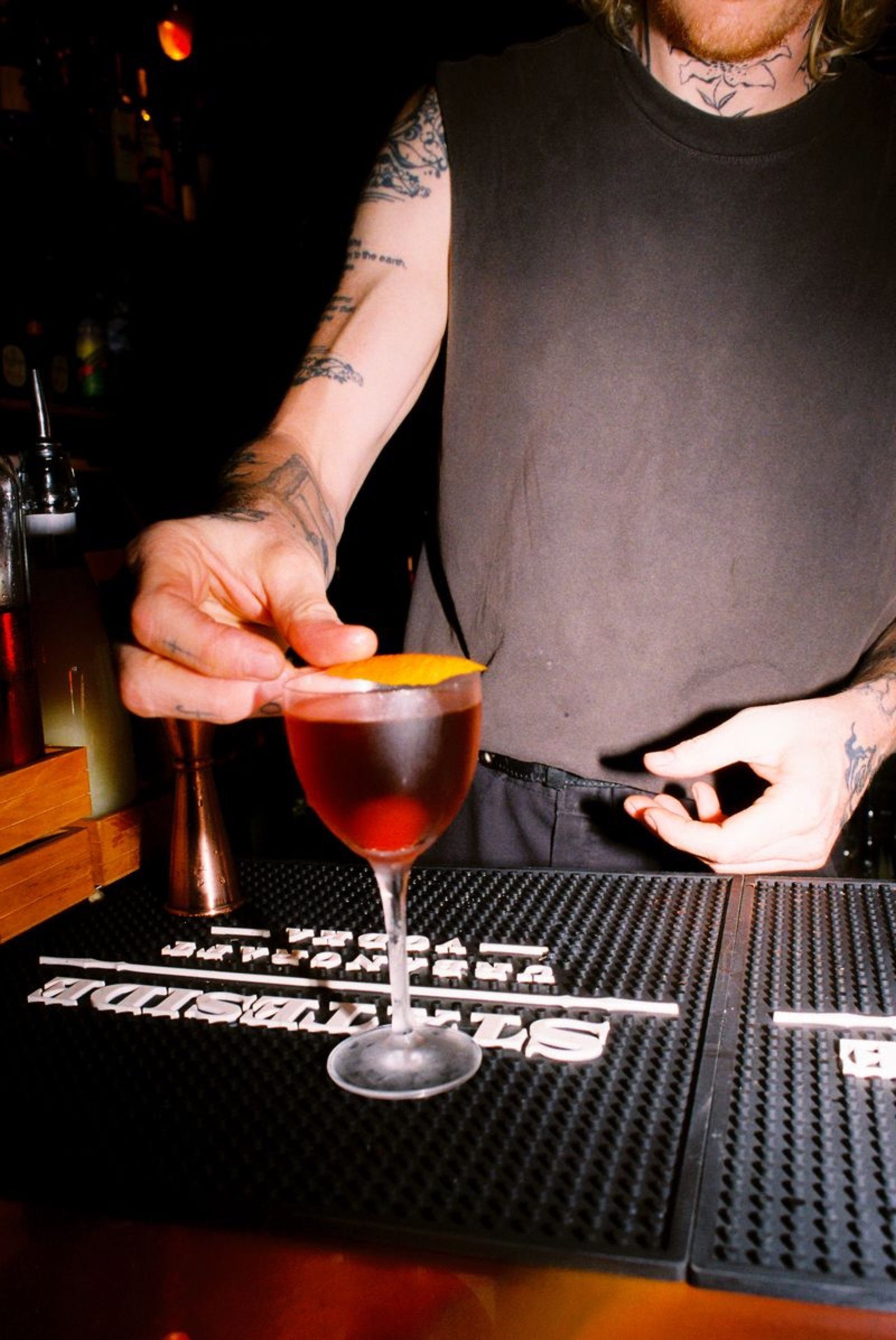 Bartender finishing a red cocktail with an orange twist on the bar mat