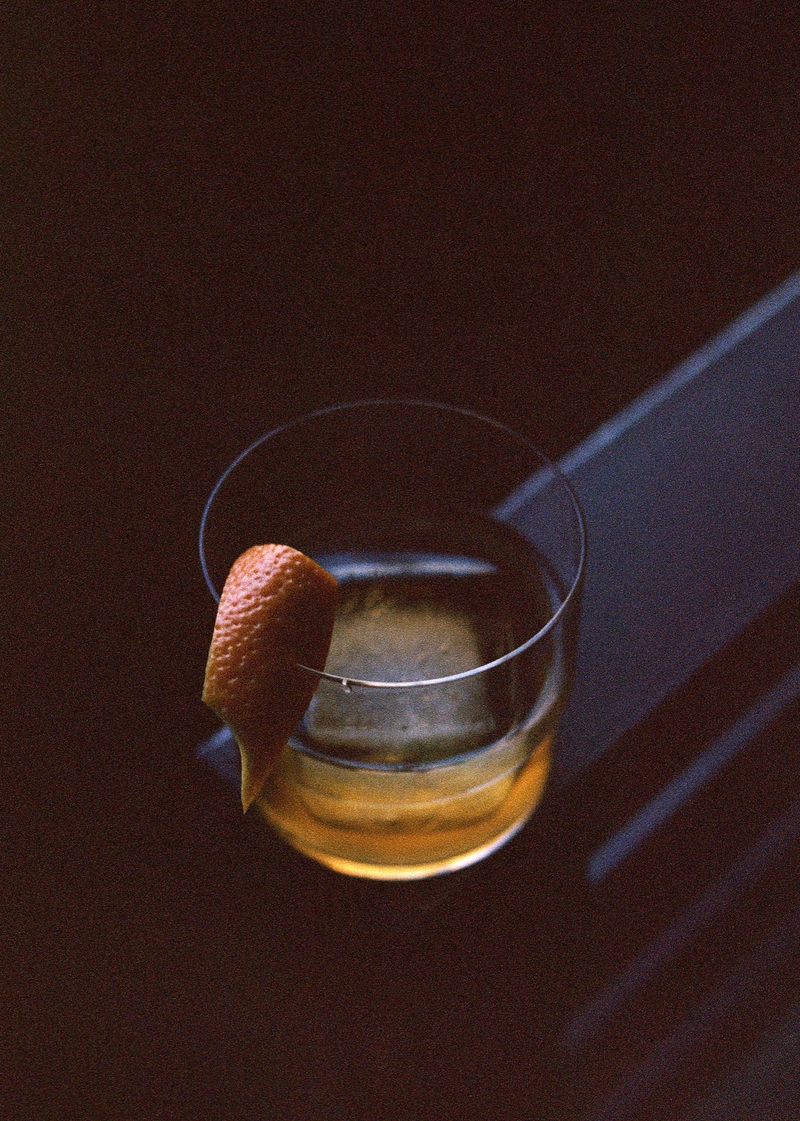 Whiskey on the rocks with an orange peel, caught in a shaft of light
