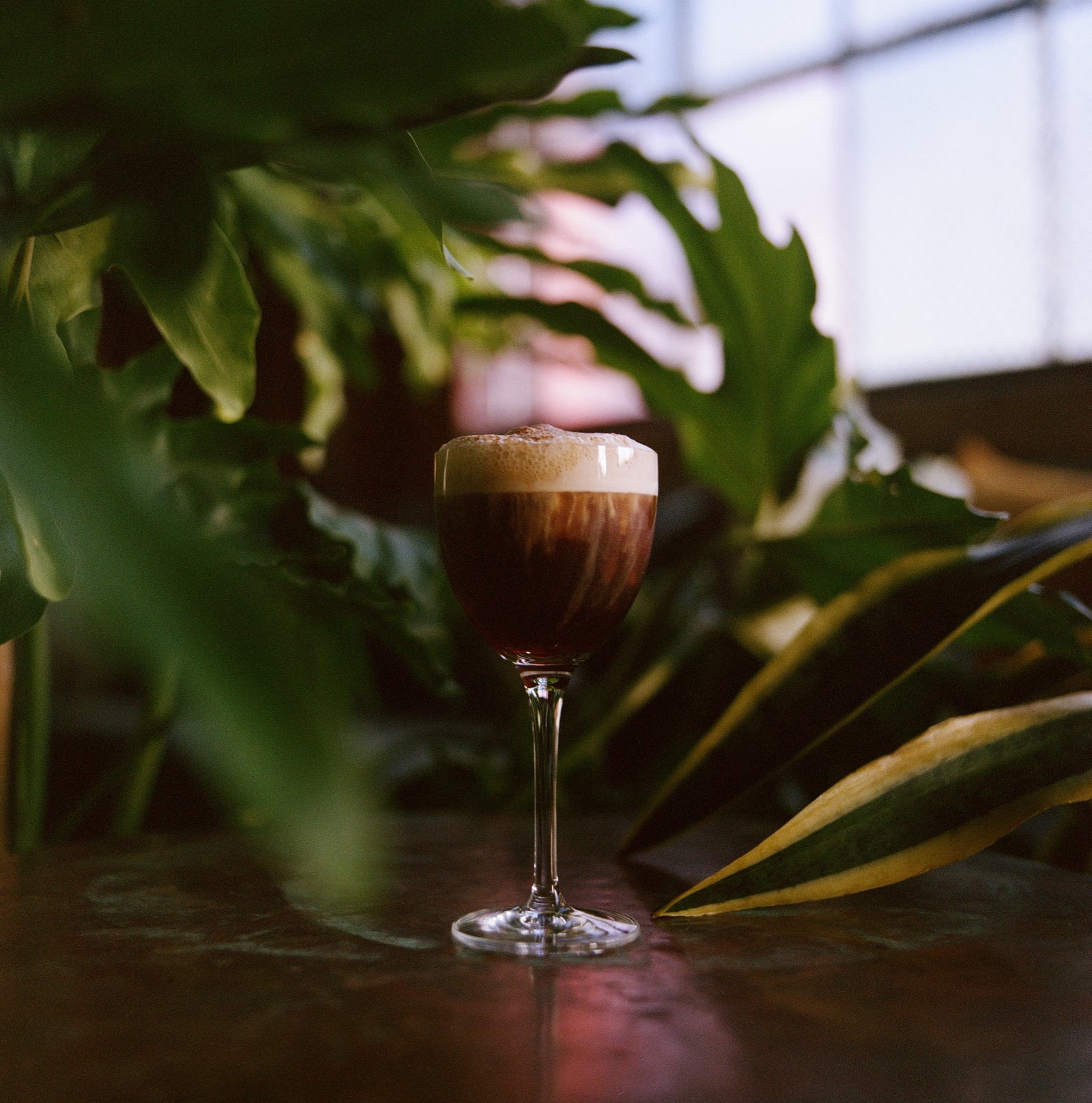 Espresso martini crowned with foam on a copper table by the window