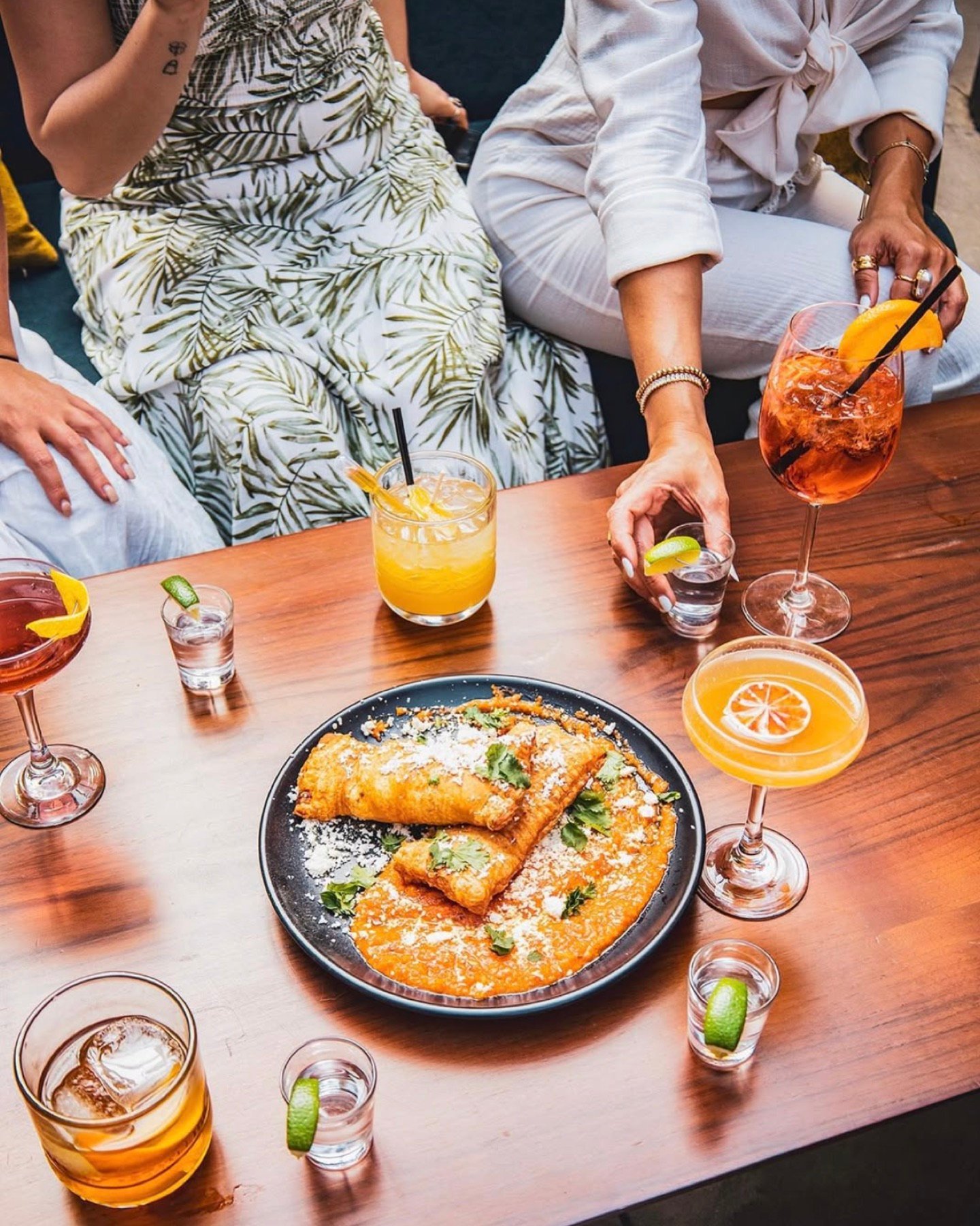 Guests sharing spritzes and a plate of empanadas at a table on The Patio