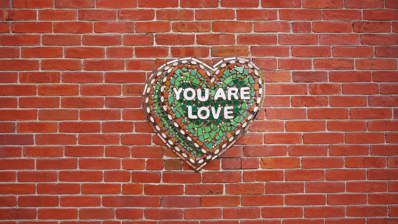 A mosaic heart reading 'You Are Love' on the brick wall at The Patio at Fabrika